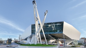 A modern building with a unique angular design and a sculpture of a car in motion.