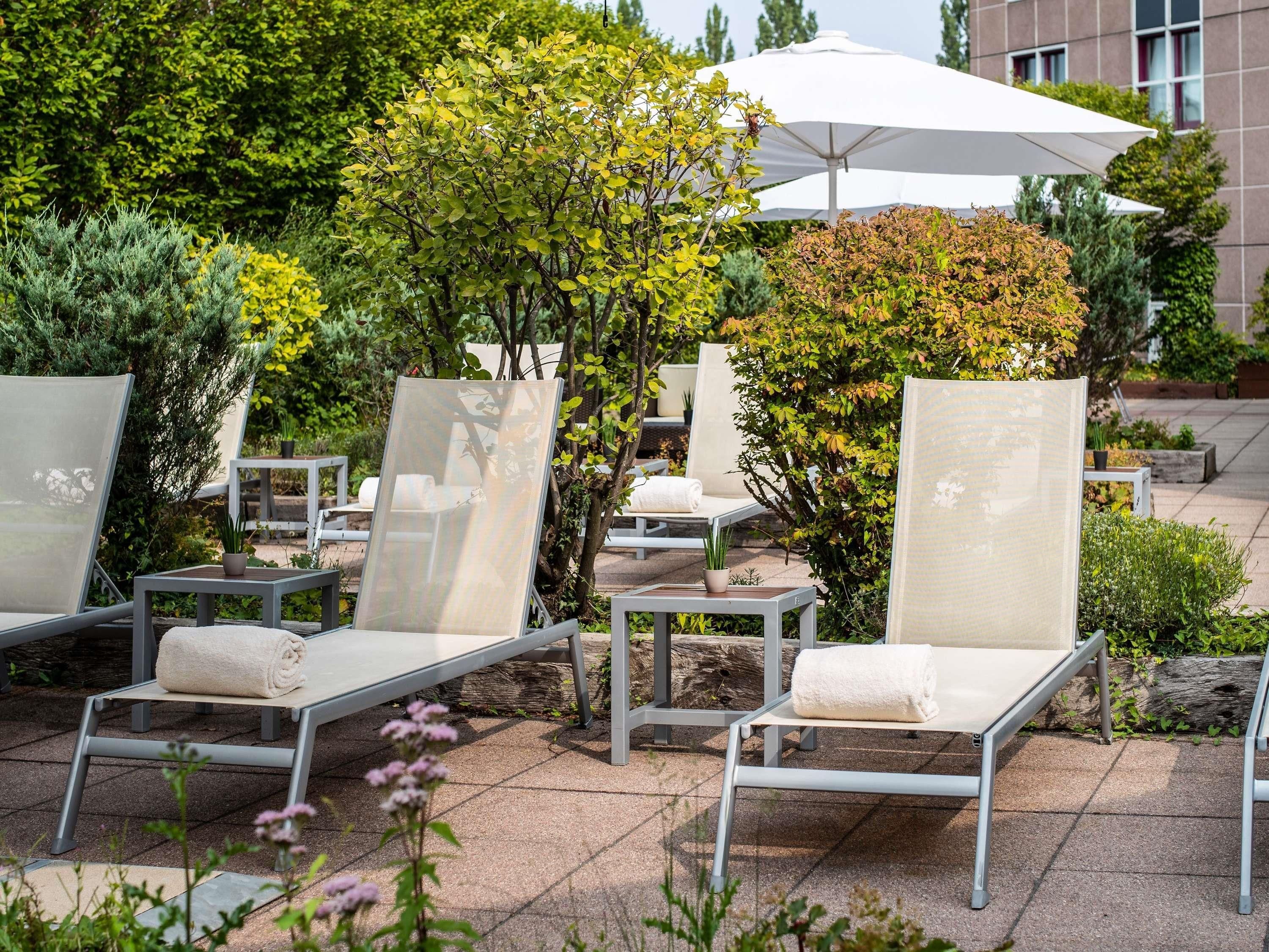 Outdoor lounge chairs with cushions, a white umbrella, and a variety of greenery in the background.
