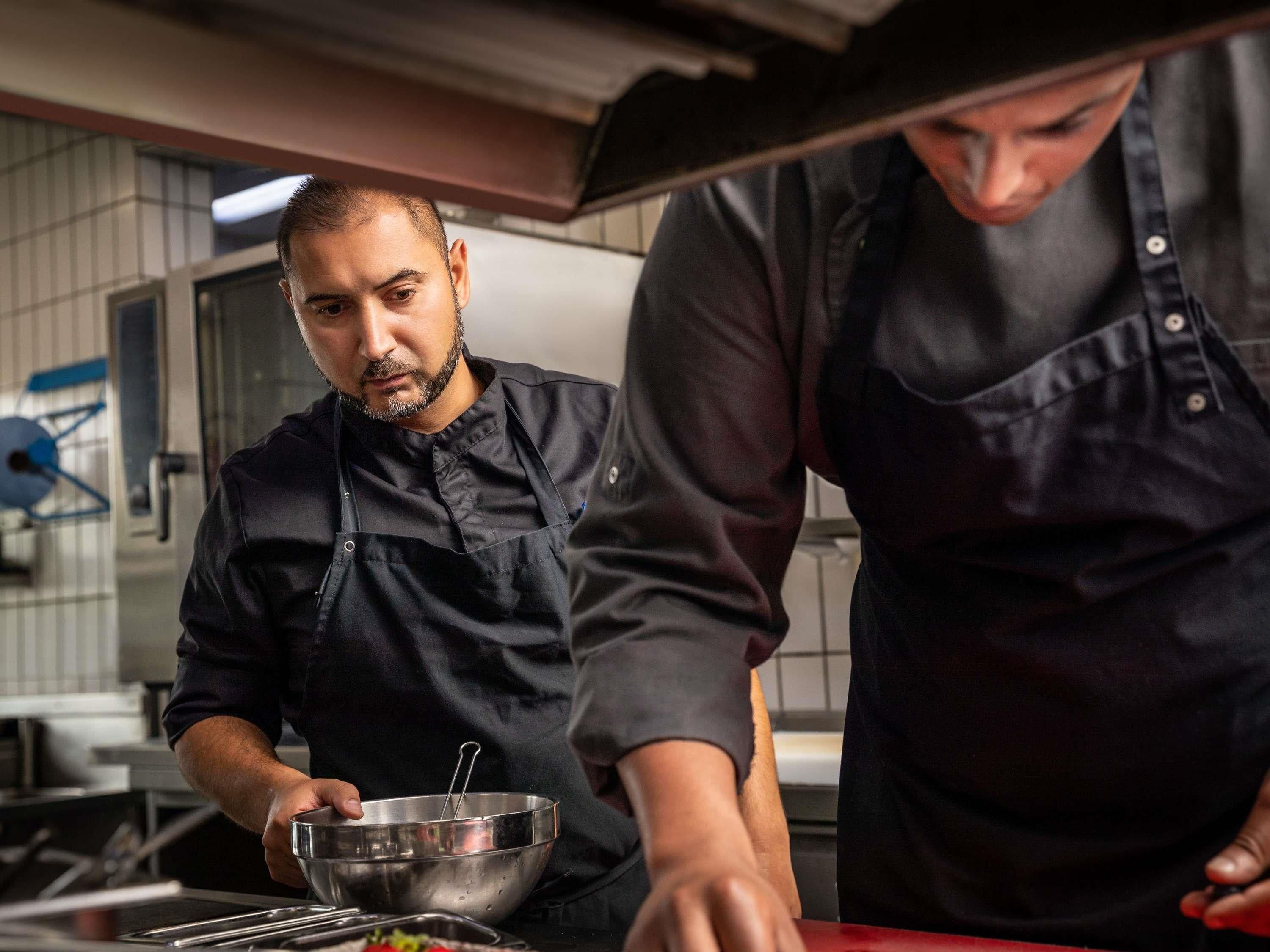 Dos personas en una cocina, una preparando comida y otra ayudando.