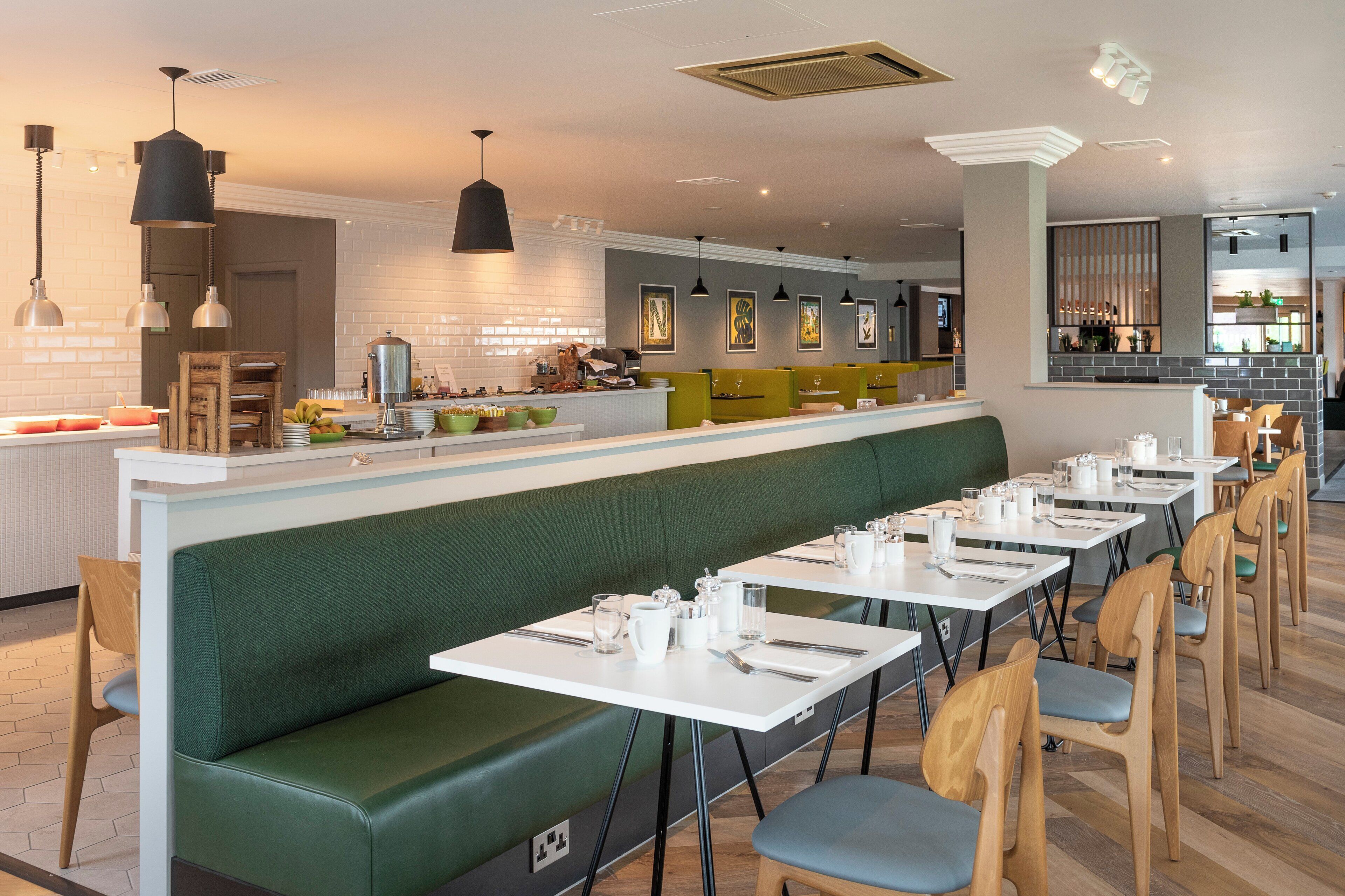 Een modern restaurant met een lange toonbank, groene zachte zitplaatsen en witte tafels.
