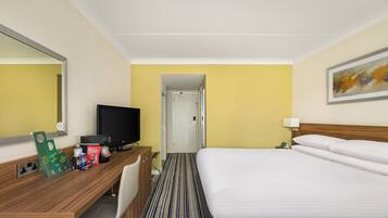 Una habitación de hotel con cama, escritorio, computadora, televisión y espejo.