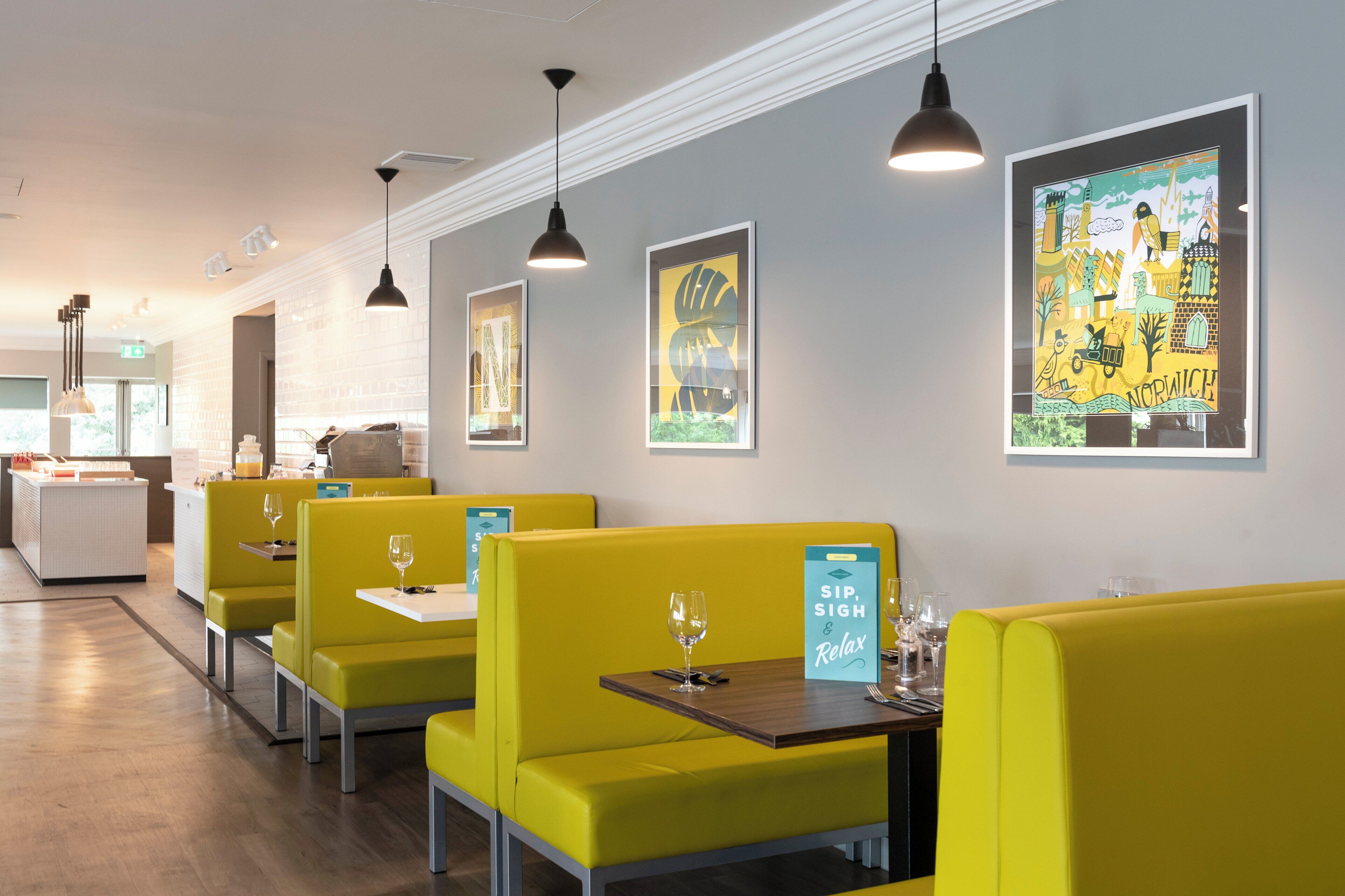 A restaurant with yellow booths, pendant lighting, and artwork on the walls.