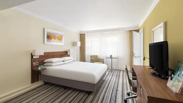 A hotel room with a bed, a desk, a television, and a window with curtains.