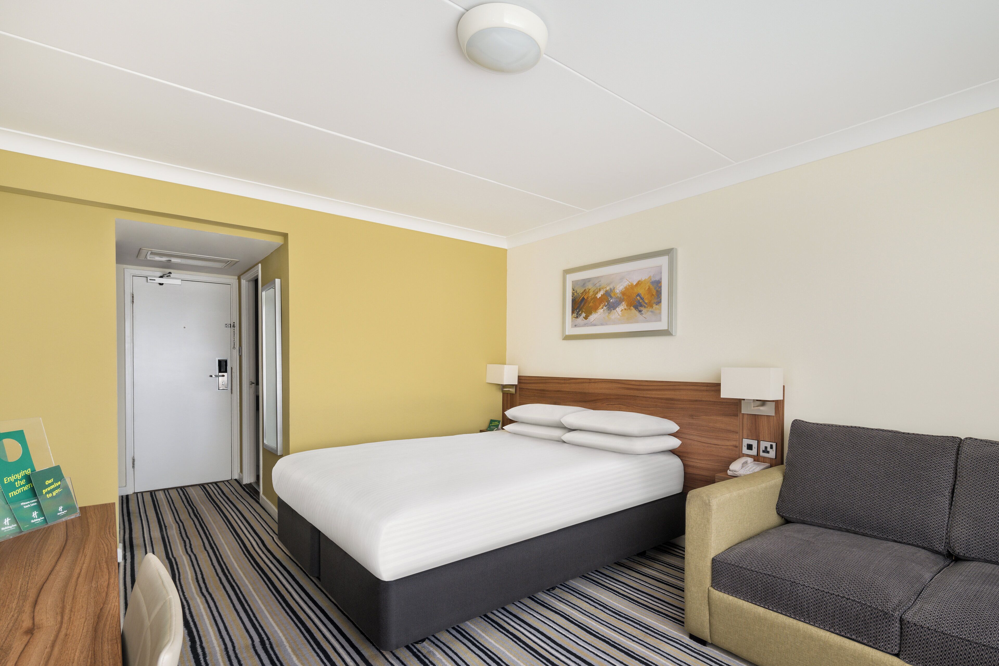 Une chambre d’hôtel avec un lit, un canapé, un tableau au mur et une porte donnant sur une autre pièce.