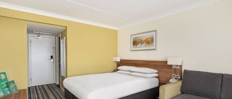 Une chambre d’hôtel avec un lit, un canapé, un tableau au mur et une porte donnant sur une autre pièce.
