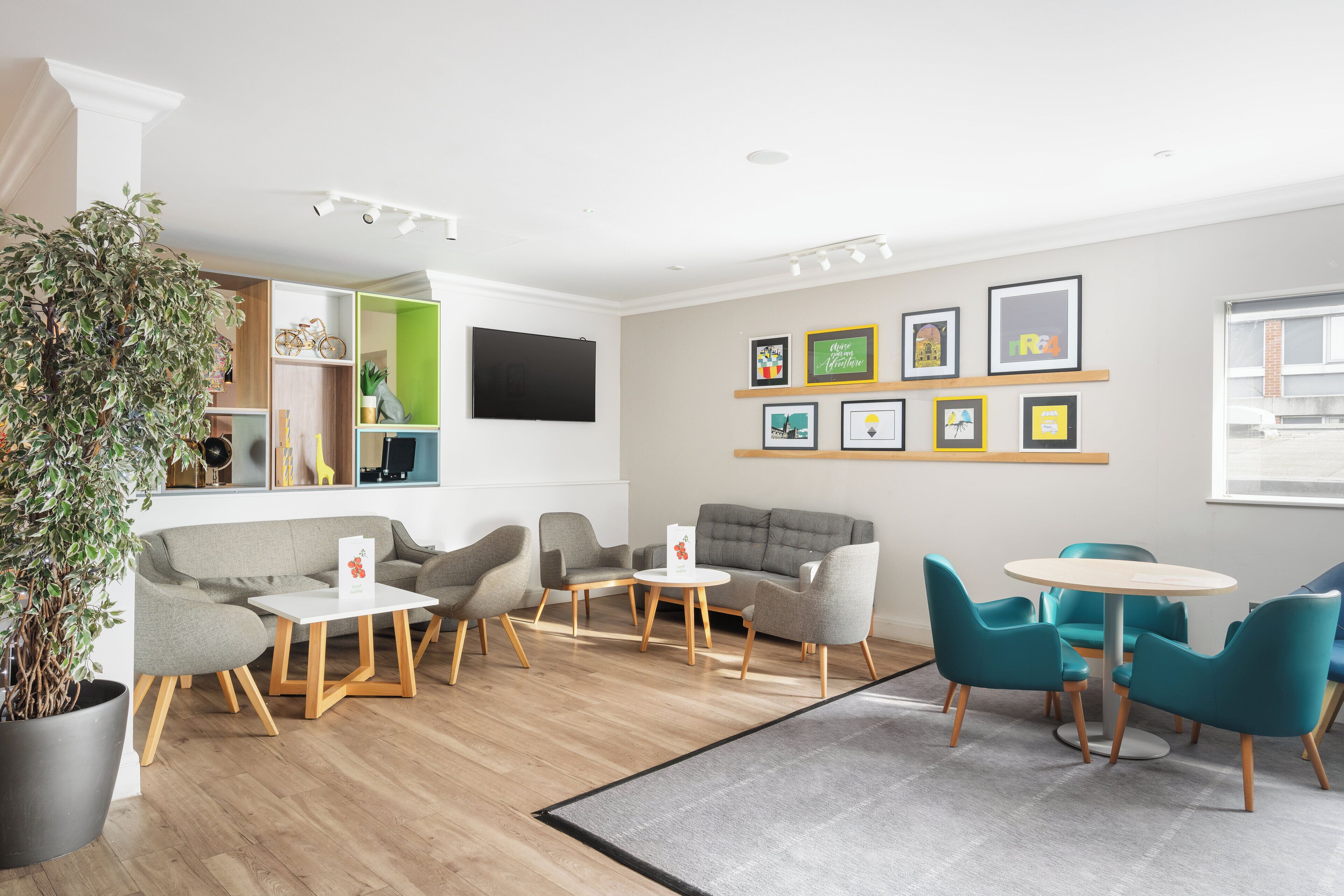 Een moderne zithoek met zitplaatsen, een bijzettafeltje, een potplant en ingekaderde foto's aan de muur.