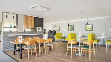 Un comedor moderno con mesas y sillas de madera, una encimera de cocina y una zona de estar con sillas amarillas.
