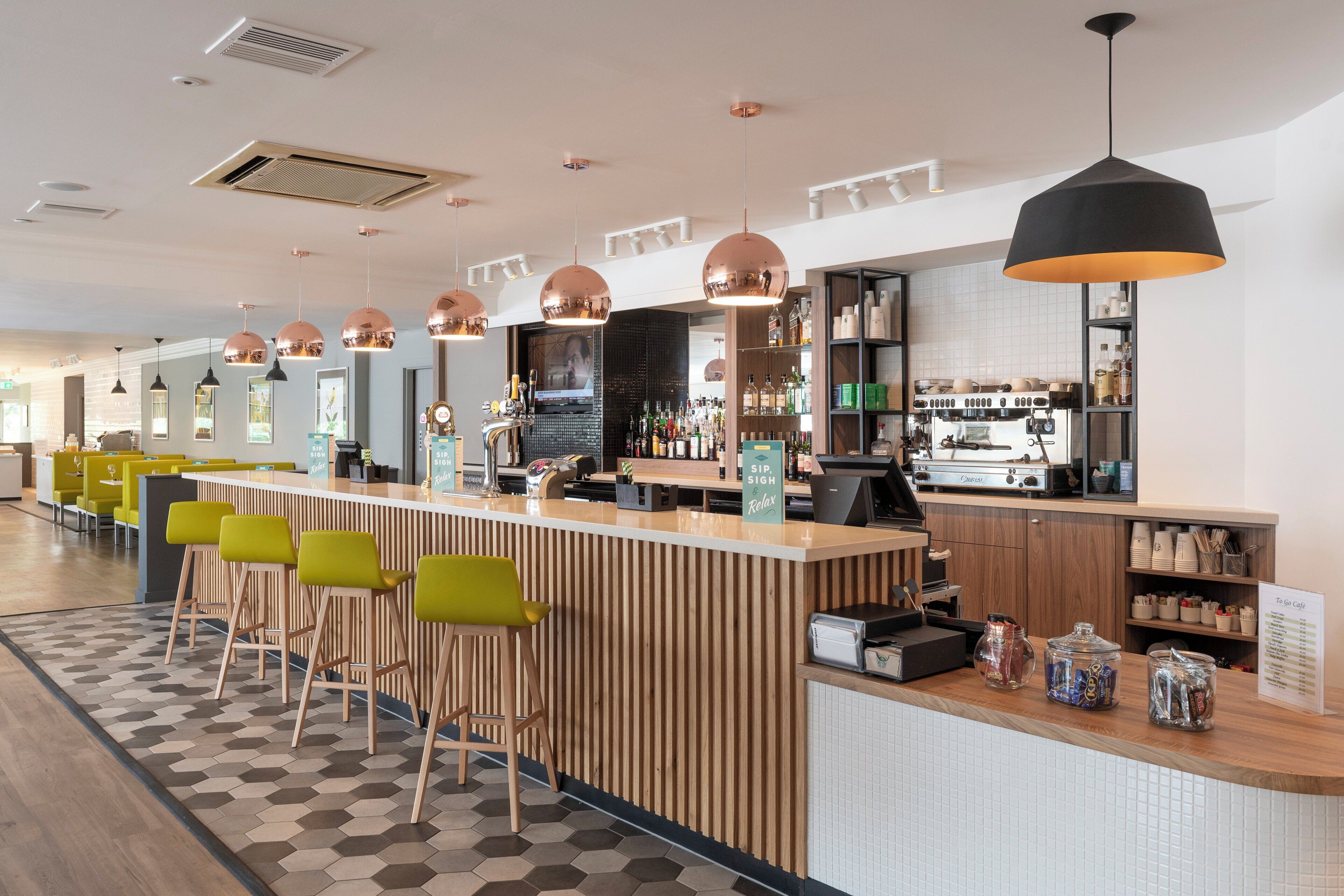 A modern bar area with a wooden counter, bar stools, and a coffee machine.