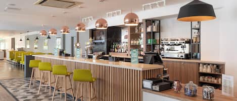 A modern bar area with a wooden counter, bar stools, and a coffee machine.
