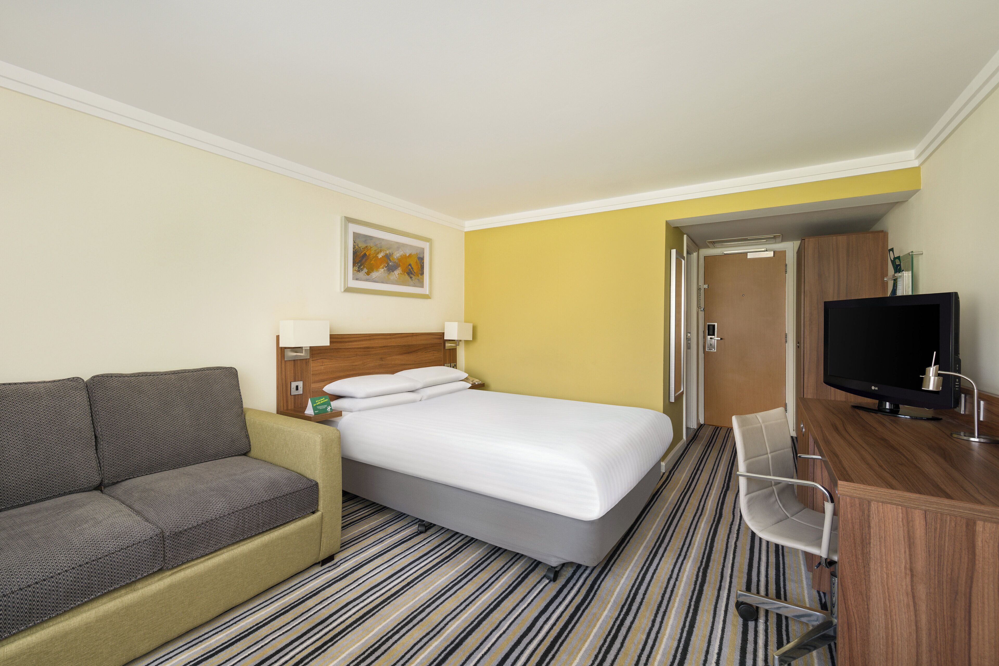 A hotel room with a bed, a sofa, a TV, and a desk.