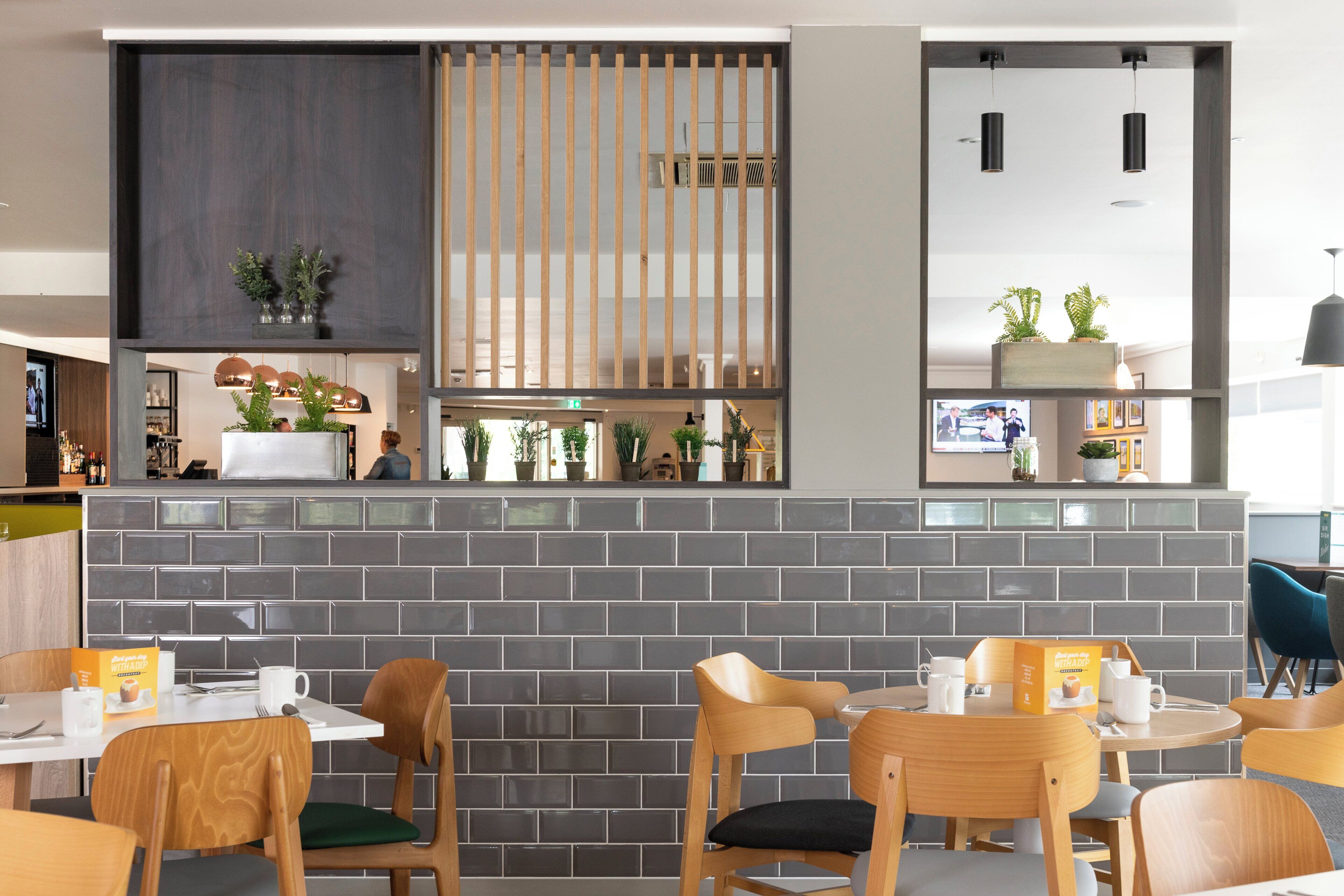 Interior moderno de una cafetería con pared de ladrillo, sillas de madera y mostrador con menú.