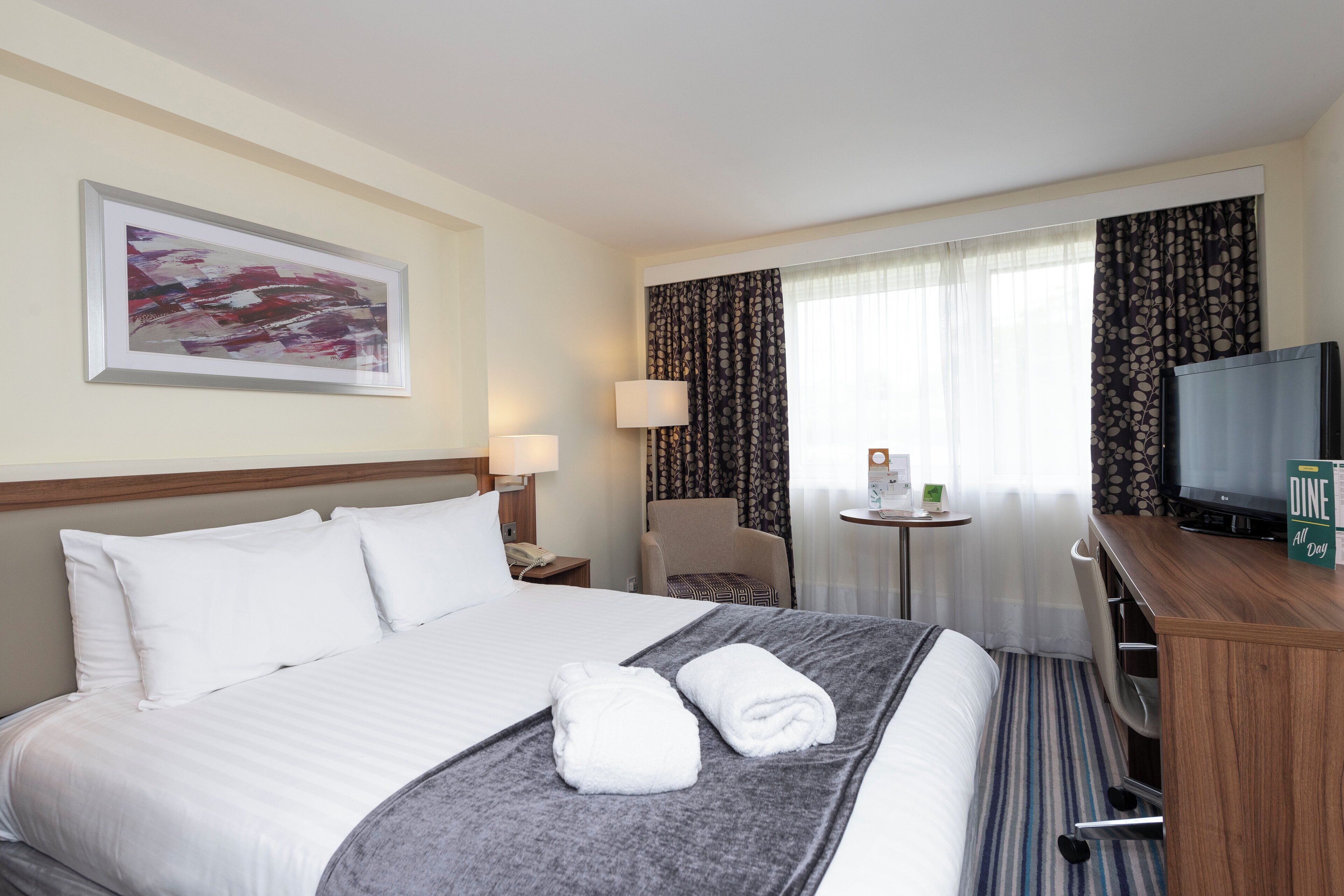 Ein Hotelzimmer mit einem Bett, einem Fernseher, einem Schreibtisch und einem Sessel.