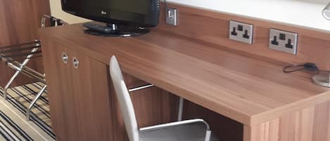 A hotel room with a wooden desk, a black LG monitor, a white office chair, and a striped carpet.