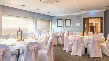 A conference room with round tables, chairs with white covers and pink bows, and framed artwork on the walls.