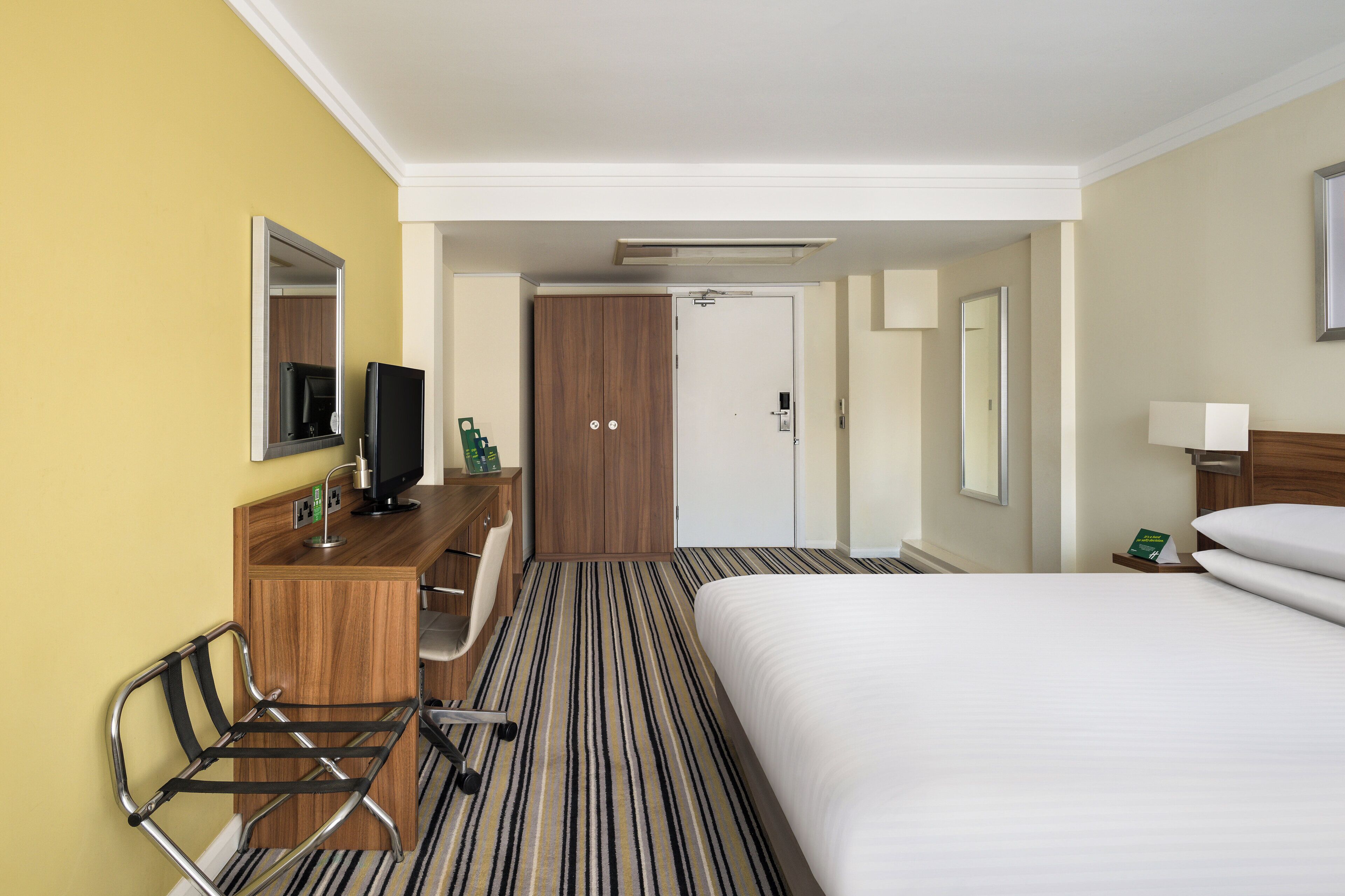 A hotel room with a bed, a desk with a chair, a television, and a wardrobe.