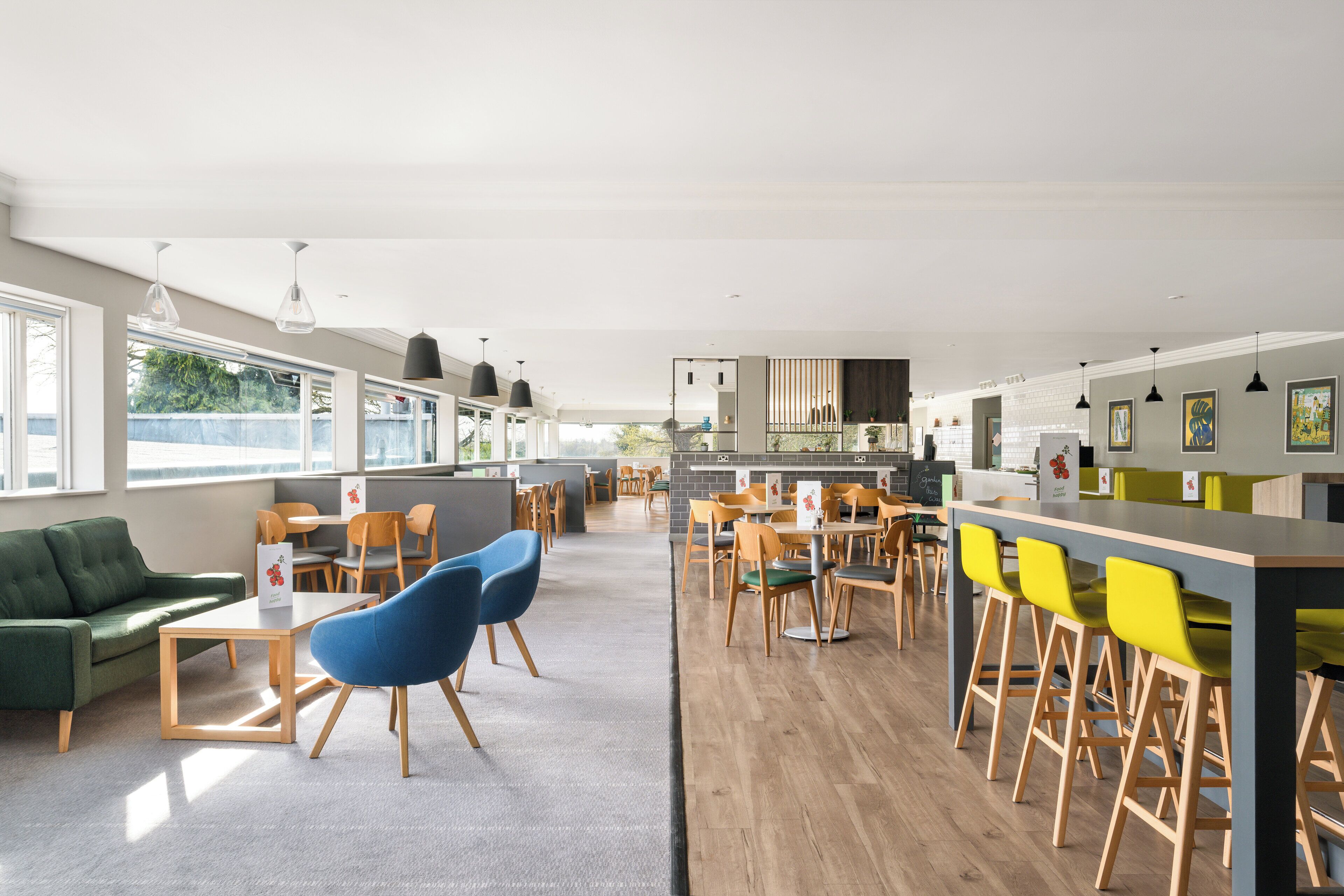 Un comedor amplio con mesas y sillas altas, un sofá verde y una cocina al fondo.