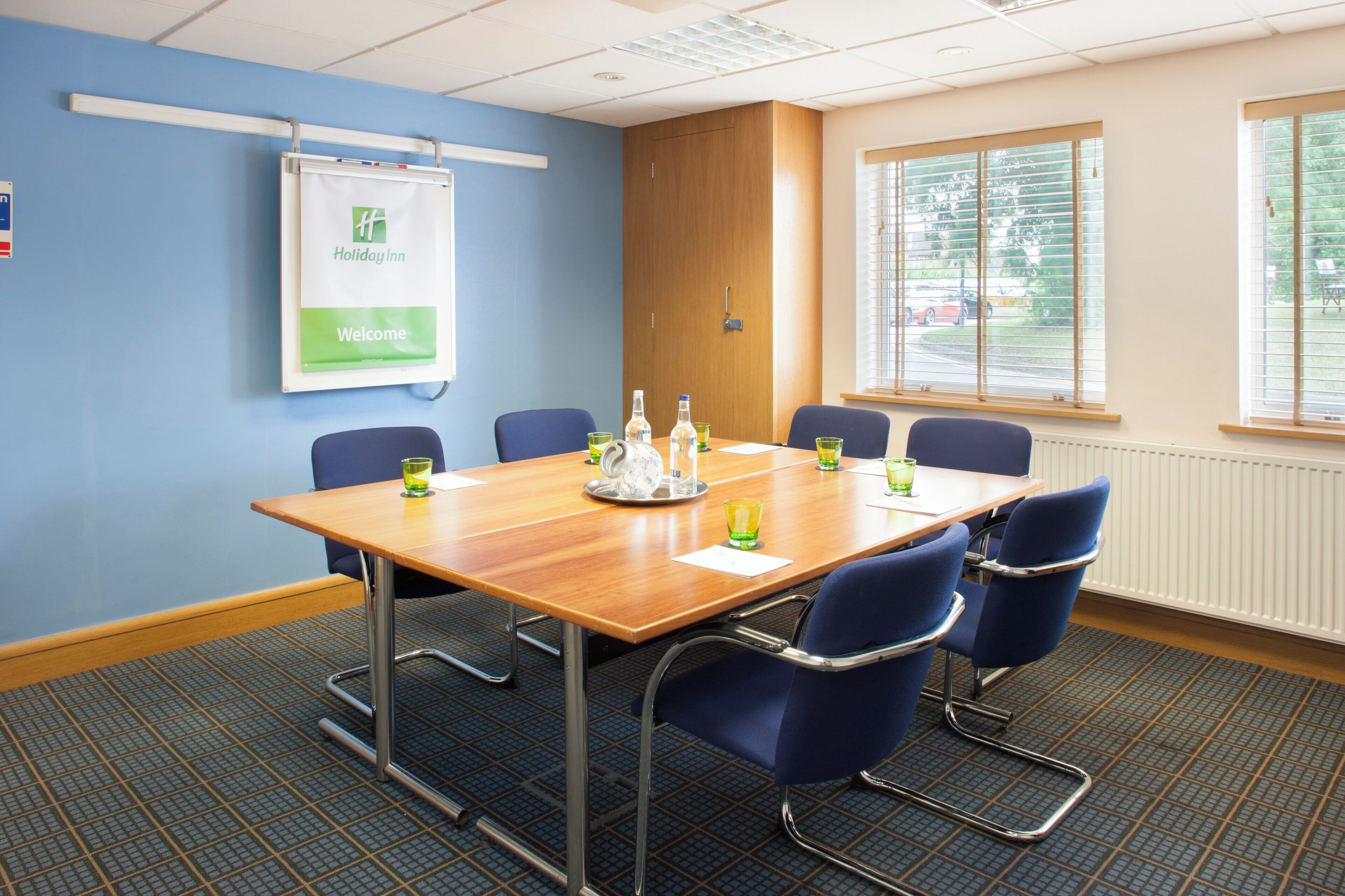 A conference room with a wooden table, blue chairs, a 'Holiday Inn' sign, and a window with blinds.