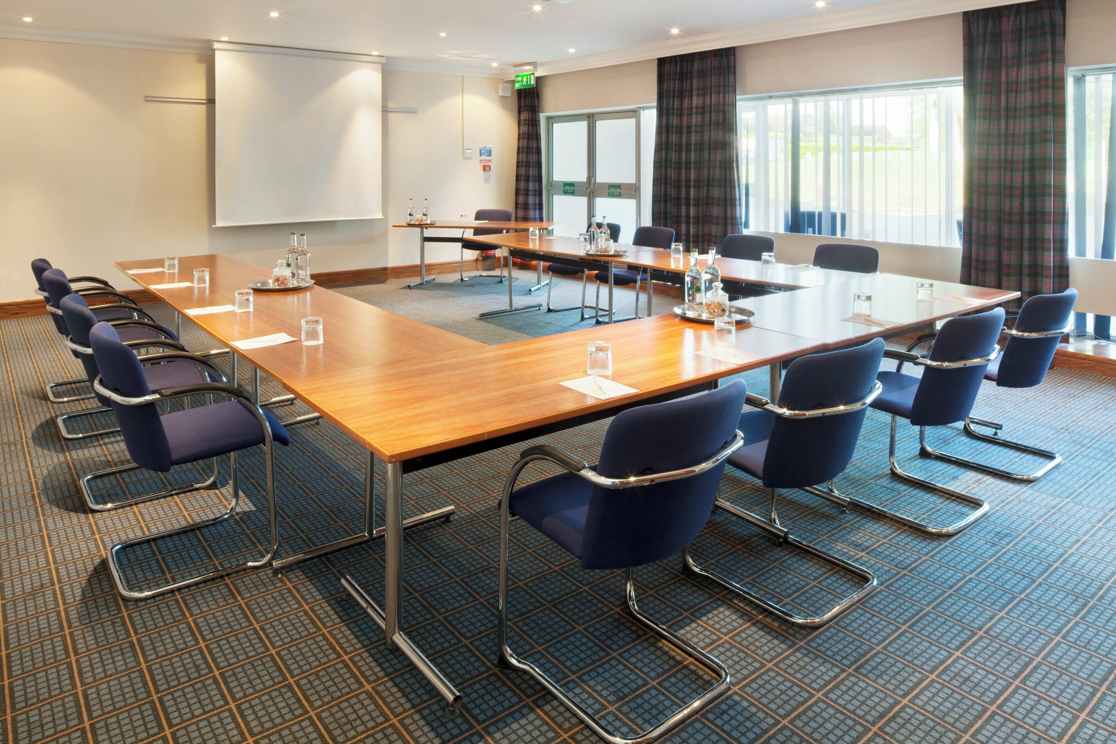 A conference room with a long table, chairs, and a projector screen.