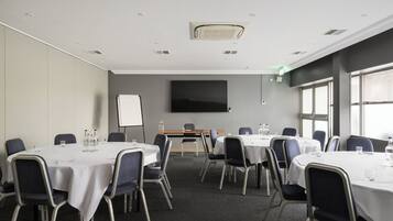 A conference room with round tables, chairs, a whiteboard, and a large flat-screen TV on the wall.