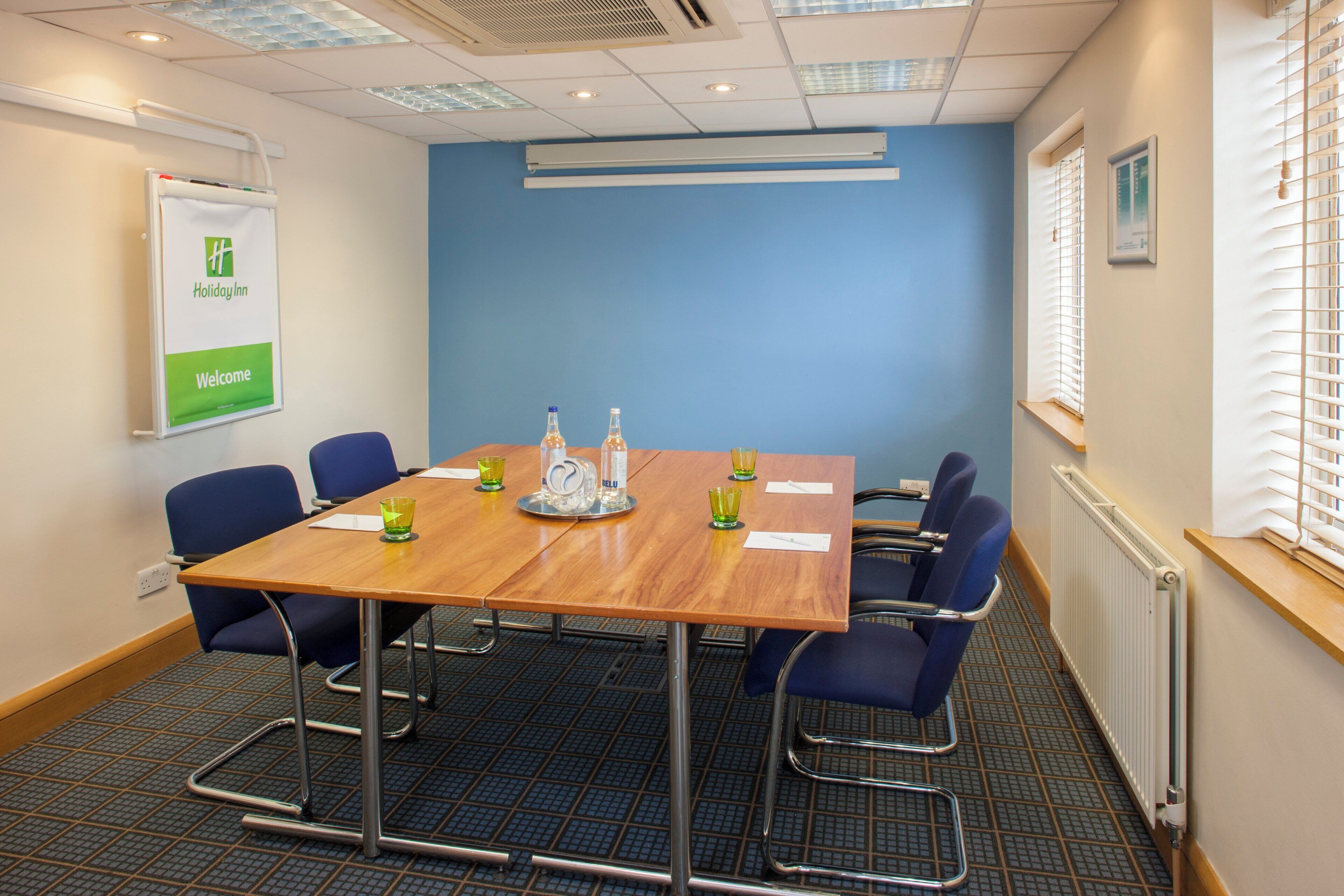 A conference room with a wooden table, blue chairs, and a whiteboard on the wall.