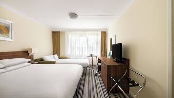 A hotel room with two beds, a desk with a TV, a small table, and a window with curtains.