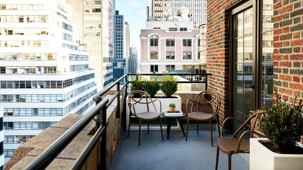 Un balcón con mesa y sillas, con vista a un paisaje urbano de edificios altos.