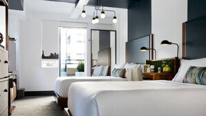 Habitación de hotel con dos camas, un espejo grande, un cabecero de madera, una mesita de noche y vistas a la silueta urbana.