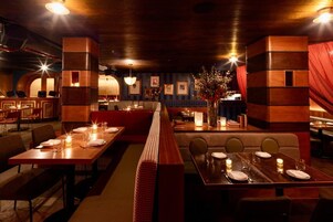 A dimly lit restaurant with wooden tables and benches, ambient lighting, and framed pictures on the walls.