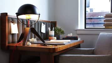 Un escritorio con una lámpara, libros, una planta y una silla en una habitación con ventana.