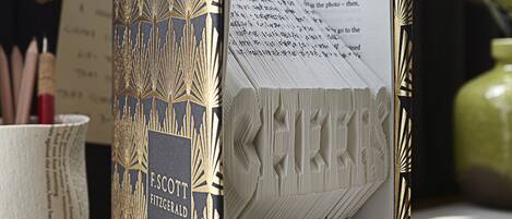 Un libro titulado "E. Scott Fitzgerald: Flappers y Filósofos" sobre una mesa, con una vista urbana al fondo.