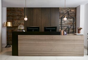 A reception desk with a wooden finish, two black monitors, and a geometric metal light fixture.