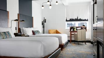 Habitación de hotel moderna con dos camas, un escritorio, una silla y vistas a la silueta urbana.