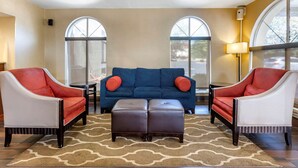 A living room with a blue sofa, two red and white armchairs, and a brown ottoman. - Comfort Inn Edison - New Brunswick (Edison)