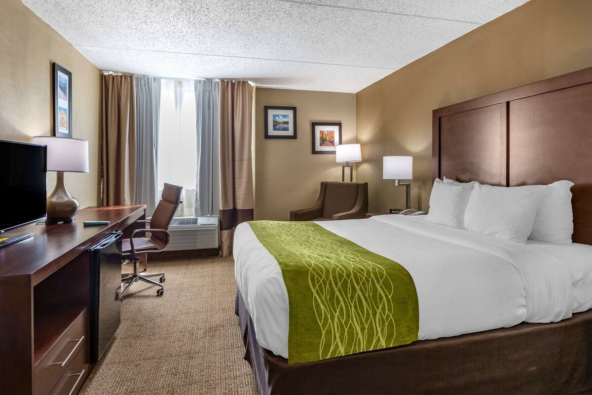 A hotel room with a large bed, a desk with a computer, a chair, and two lamps.