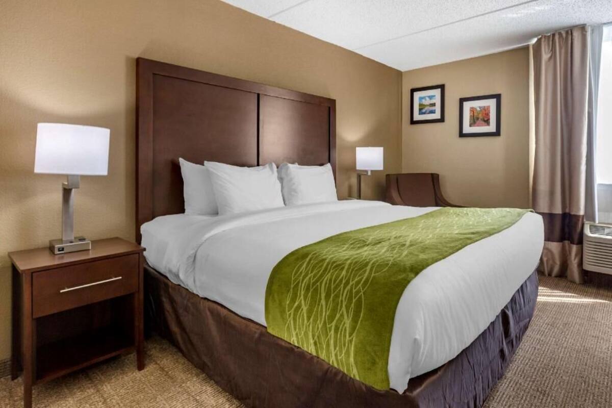 A hotel room with a large bed, two bedside tables, a nightstand, a green throw blanket, and two framed pictures on the wall.