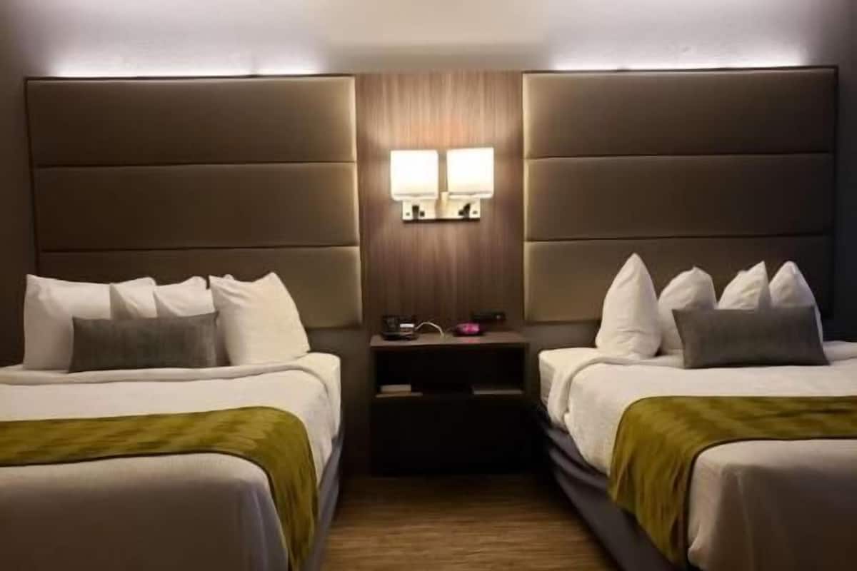 A hotel room with two beds, a wooden headboard, a nightstand with a lamp, and a small table.