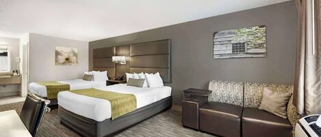 A hotel room with two beds, a sofa, a desk, and a bathroom.