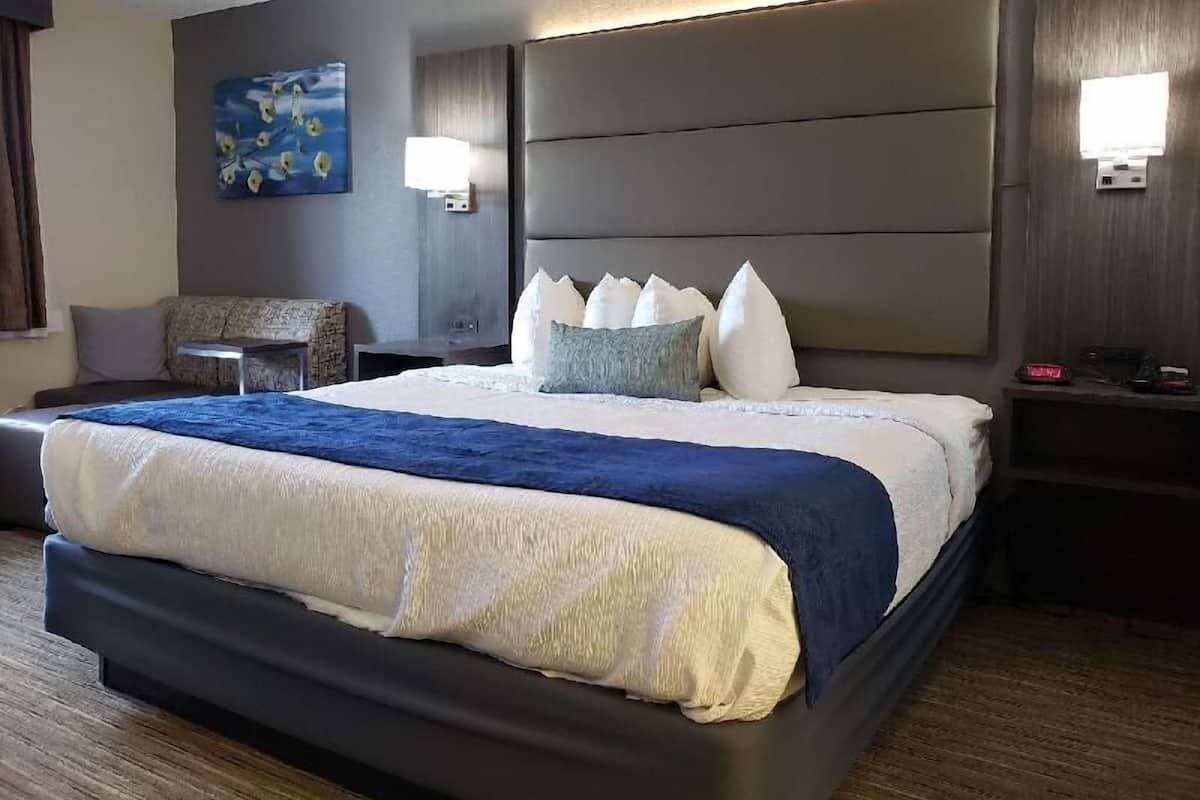 A modern hotel room with a large bed, a seating area, and a painting on the wall.