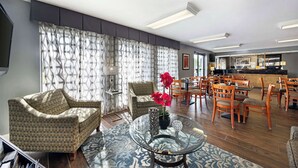 A living room with a sofa, chairs, a glass coffee table, and a dining area with wooden chairs and a table.