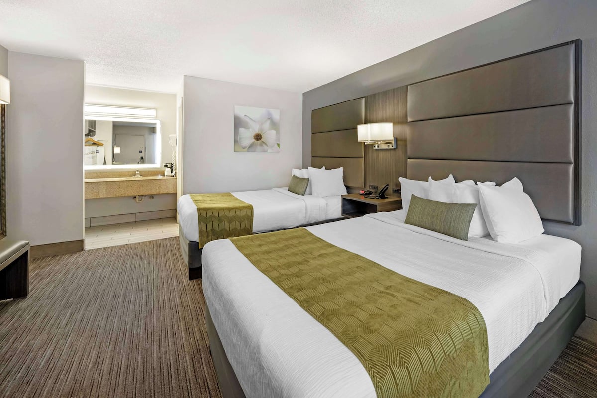 A hotel room with two beds, a large mirror, a bedside table with a lamp, and a wall-mounted light fixture.