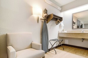 A hotel bathroom with a beige armchair, a towel rack, a mirror, and a sink. - Red Roof Inn Durham - Duke Univ Medical Center (Durham)