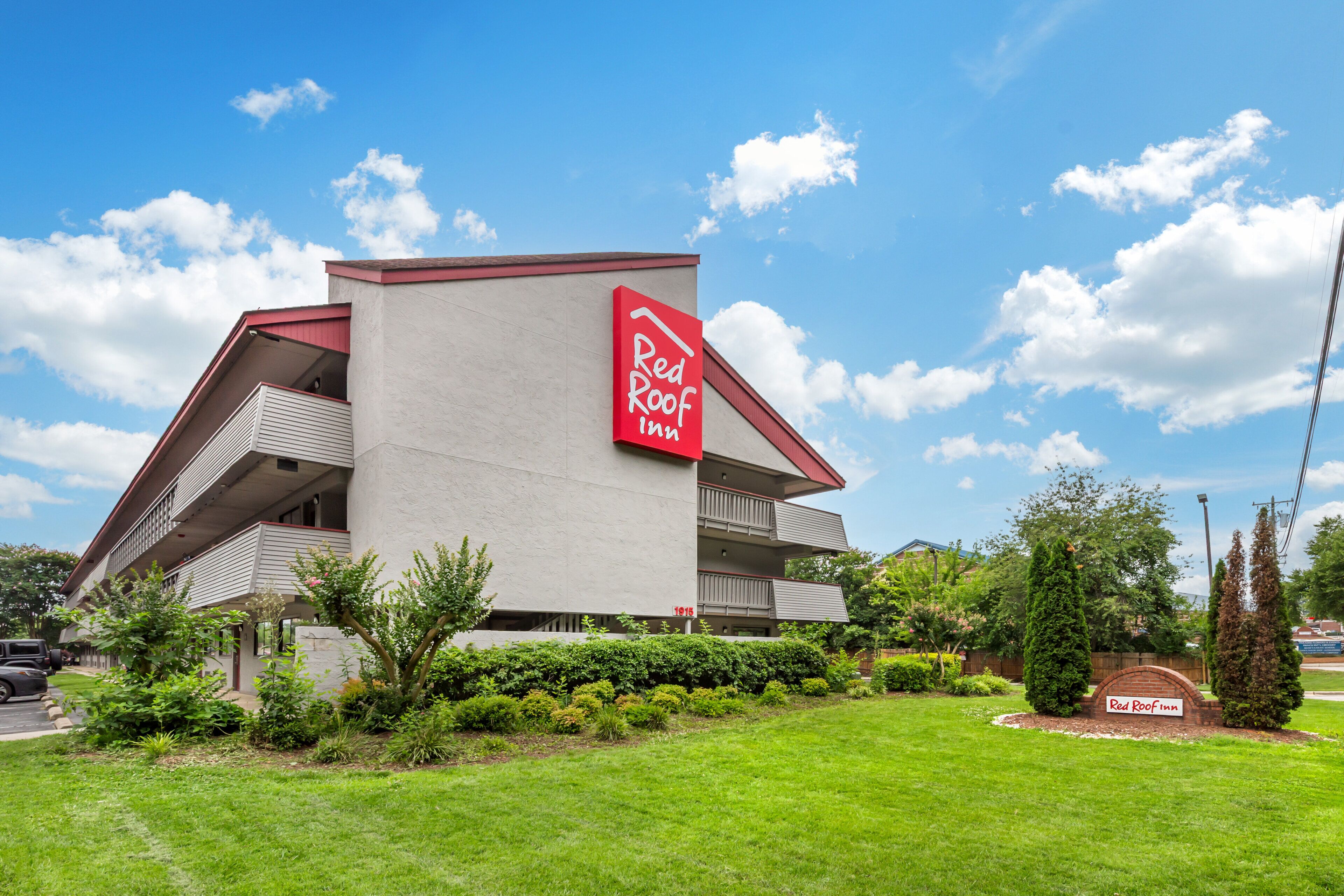 A Red Roof Inn with a modern architectural design, featuring a prominent red and white sign, a well-maintained lawn, and a parking area.