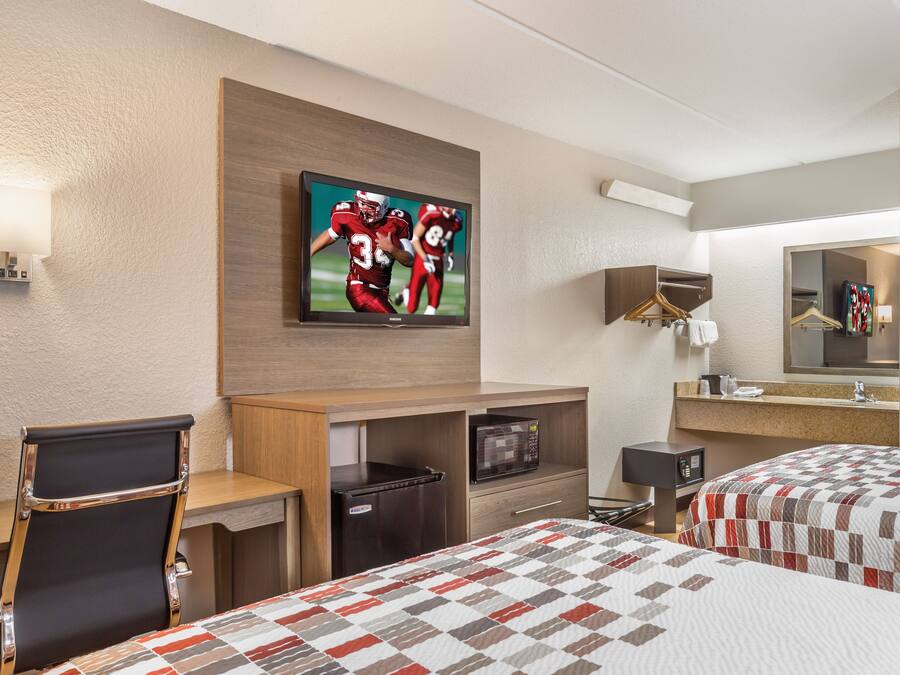 A hotel room with a bed, a desk, a chair, a television, a microwave, a refrigerator, and a mirror.