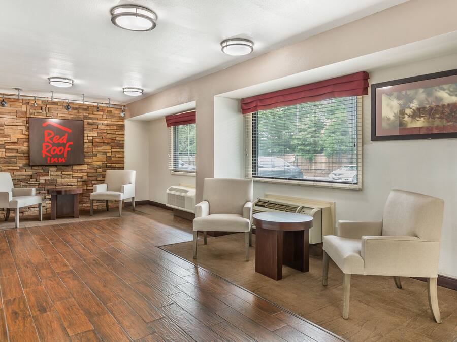 A Red Roof Inn lobby with a stone wall, wooden flooring, and a seating area with chairs and a small table.