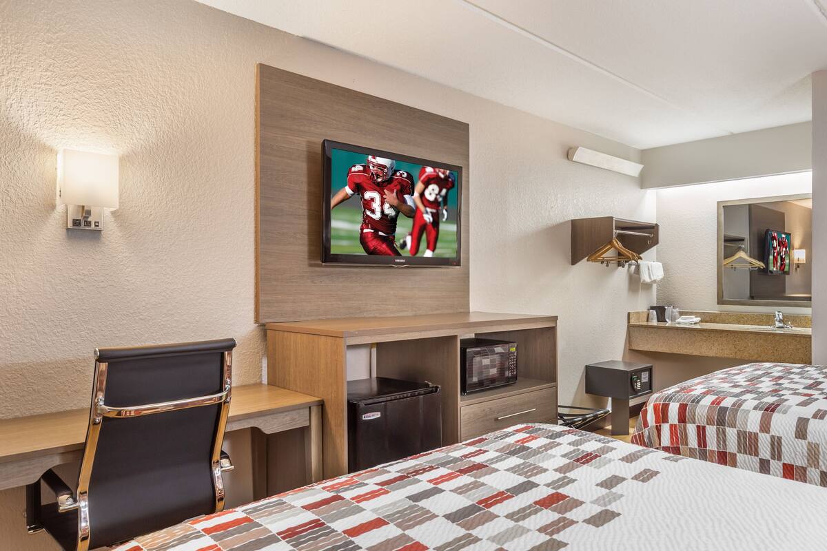 A hotel room with a bed, a desk, a chair, a television, a microwave, a refrigerator, and a mirror.