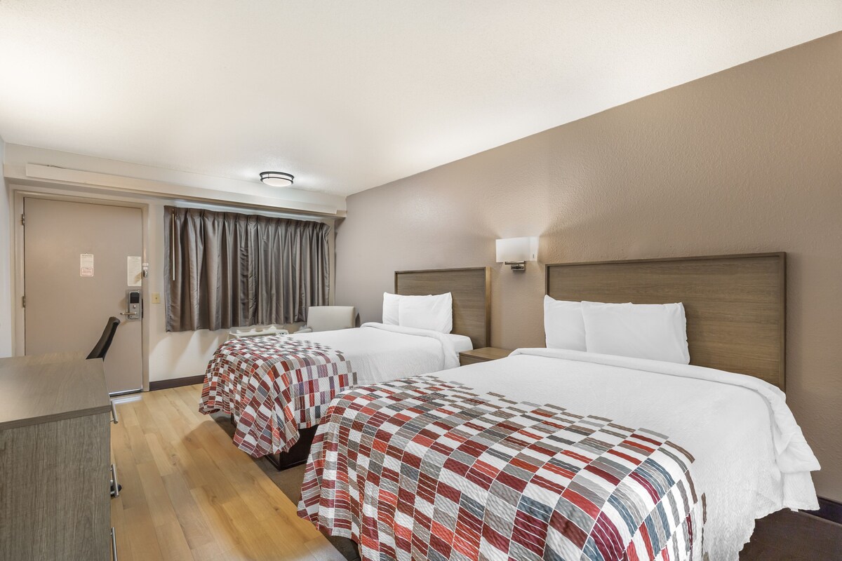 A hotel room with two beds, a desk, and a chair.
