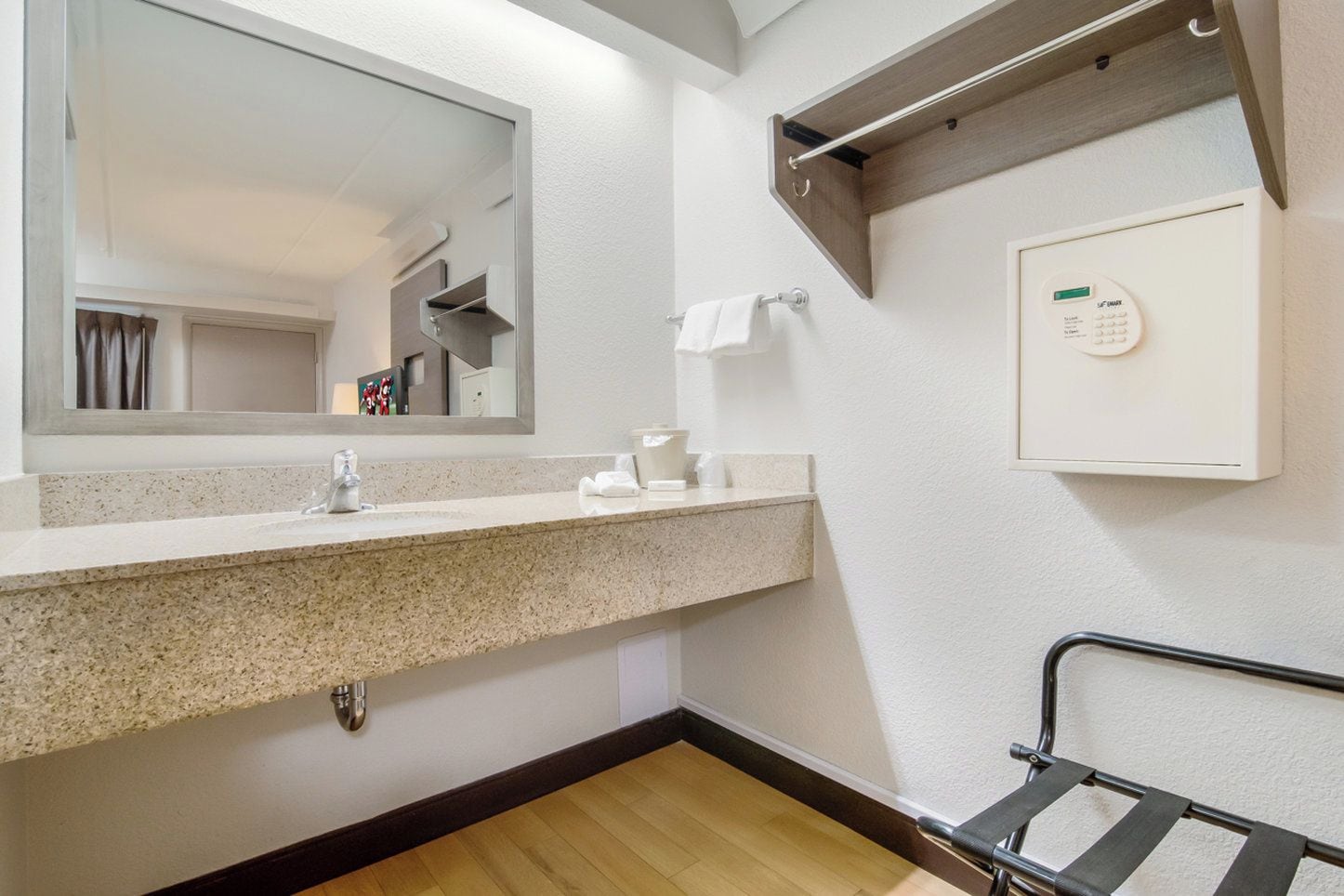 A bathroom with a granite countertop, a mirror, a towel rack, a towel, a soap dispenser, and a wall-mounted thermostat.