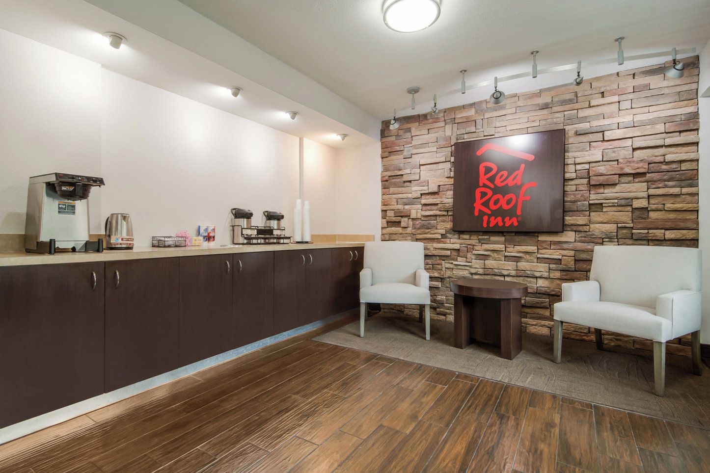 L'espace d'accueil d'un hôtel Red Roof Inn, avec un mur en pierre, une machine à café et deux fauteuils blancs.