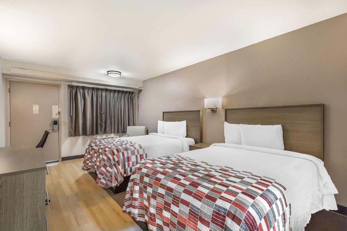A hotel room with two beds, a desk, and a chair.