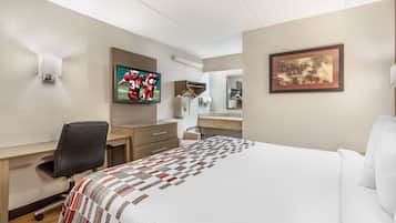 A hotel room with a bed, a desk, a chair, a television, a mirror, and a framed picture on the wall.